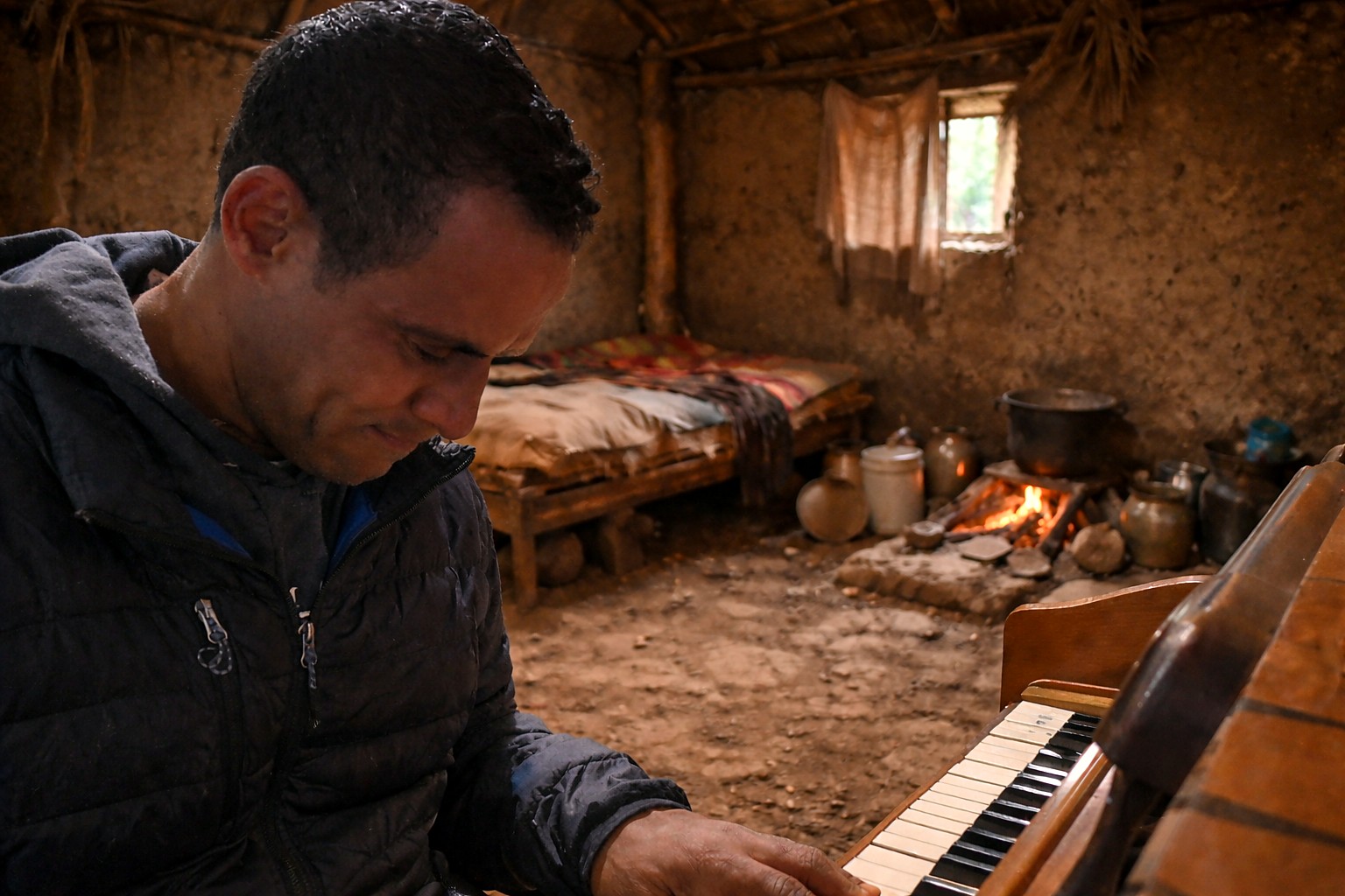 Dereje Desta playing piano in an earthen-walled hut, fire burning